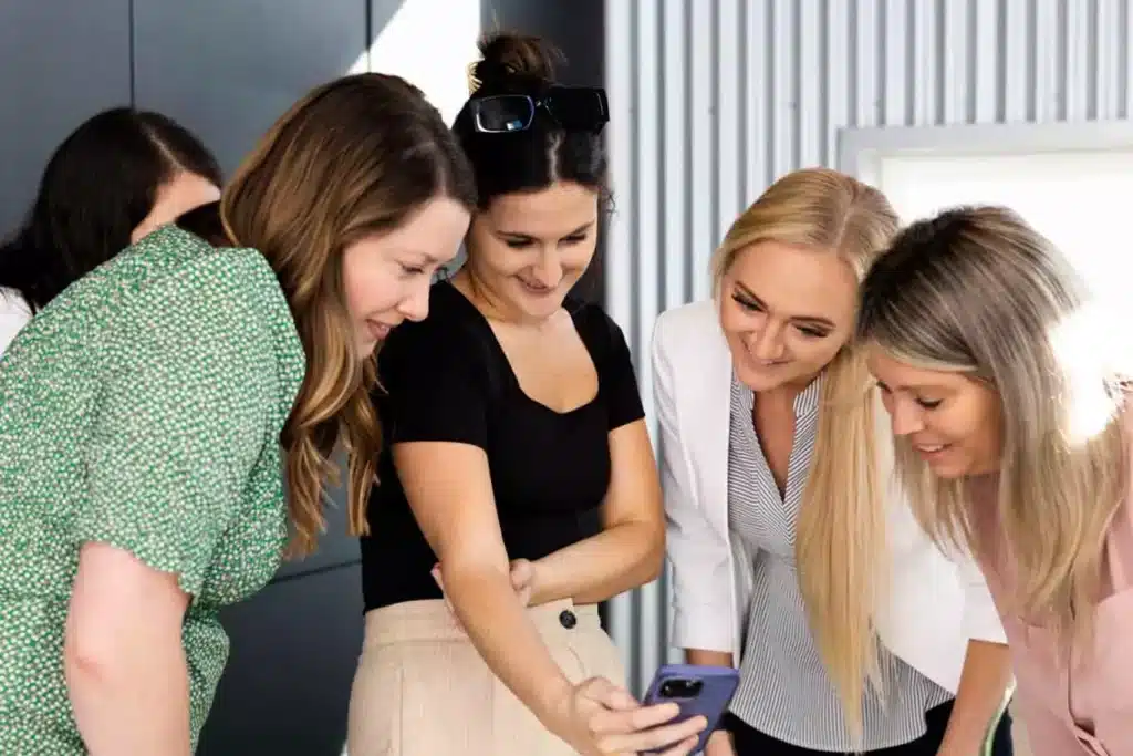 group of women surrounding a phone smiling